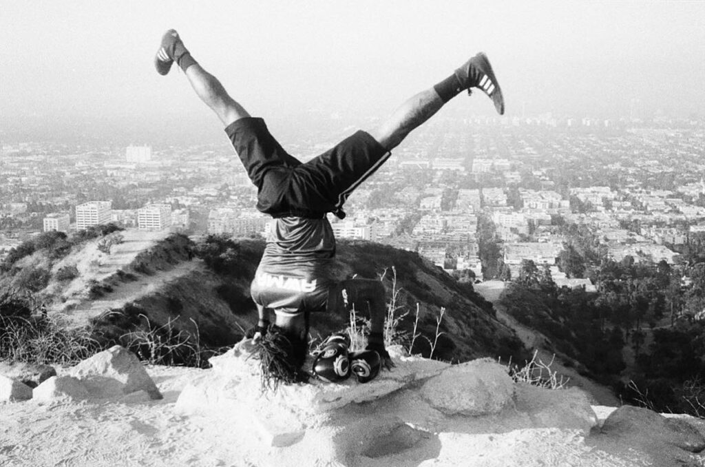 martial arts travel in action. a man does a headstand in martial arts gear, looking over a valley below. 